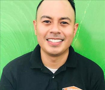 Young man with dark hair and a big smile, wearing a green, SERVPRO labeled golf shirt.