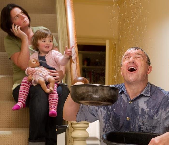 A man holding pans catching water falling. Woman sitting on stairs holding a child on the phone.