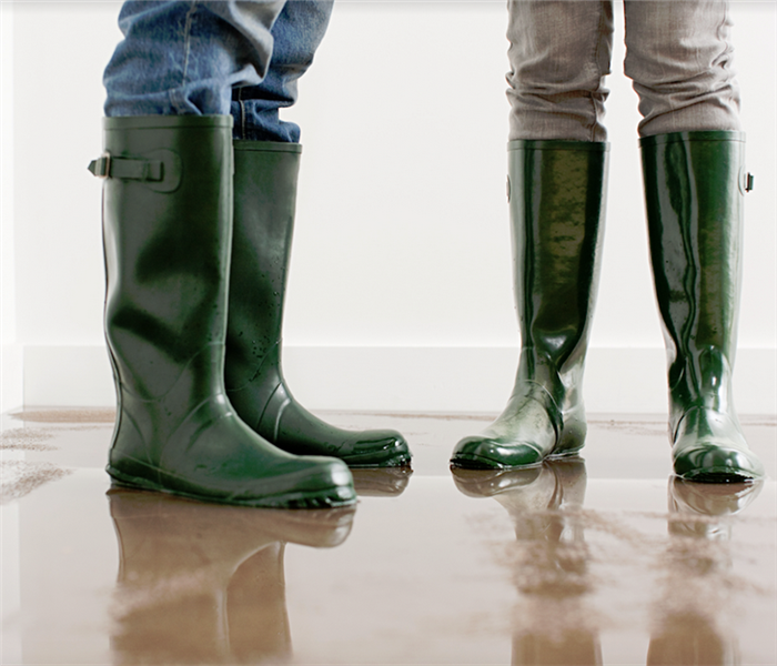 two people standing in a flooded room in rain boots 