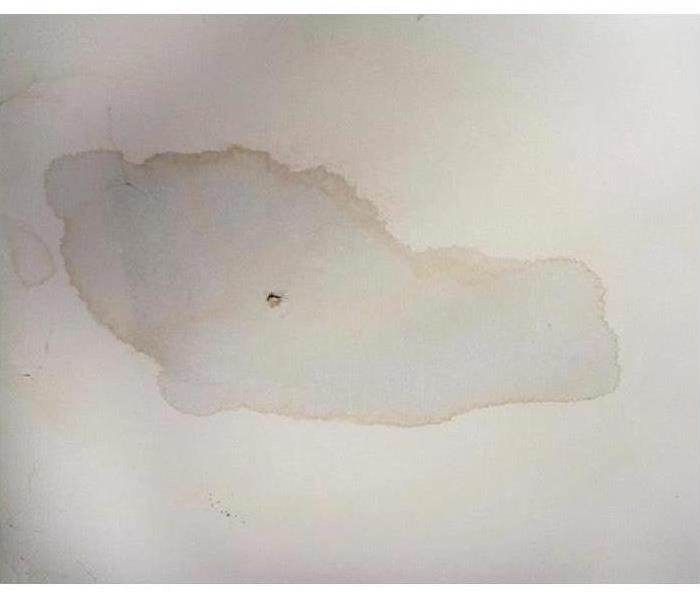 A white ceiling with a light brown water stain. 