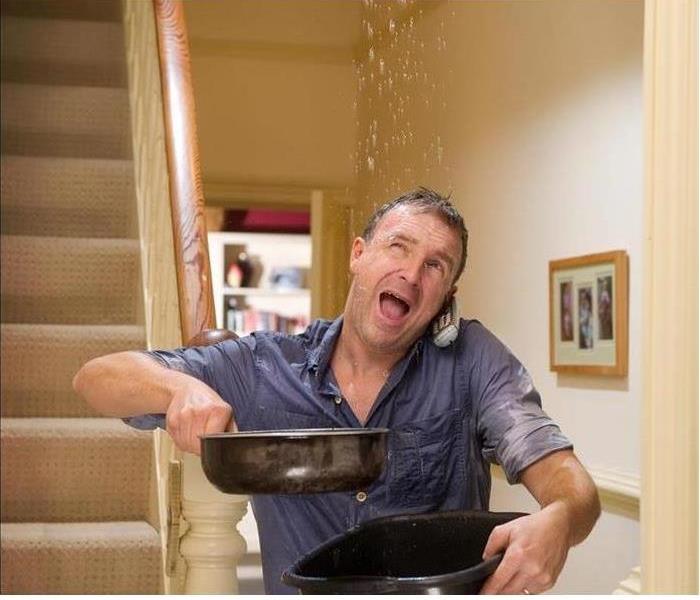man catching ceiling water leak with pans