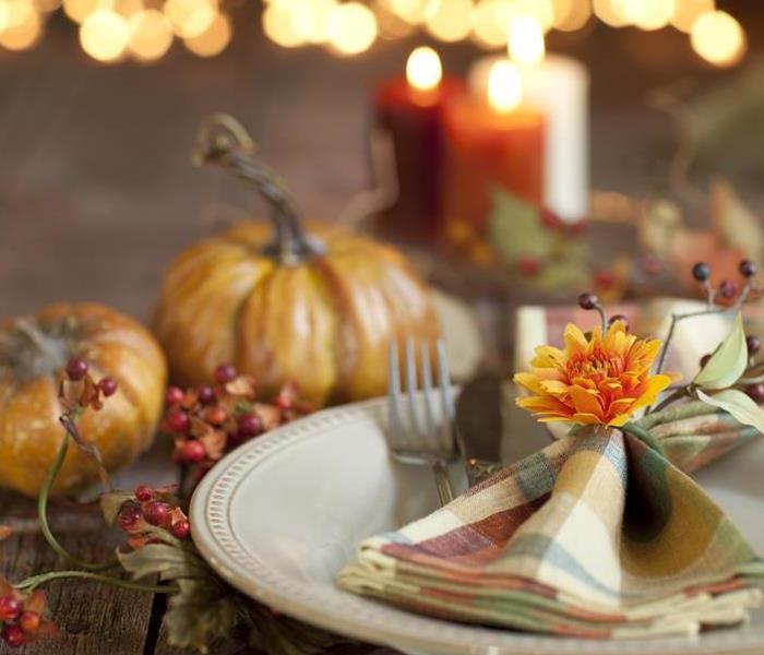 A fall decorative dinner plate set, with pumpkins, and candles burning in the background. 